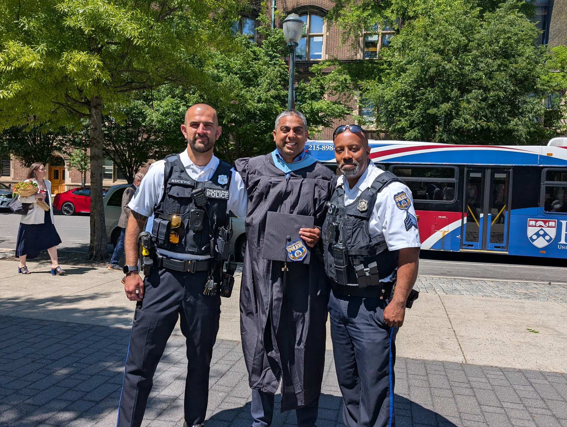 Philip Singh in academic regalia with two Philadelphia Police officers at University of Pennsylvania commencement